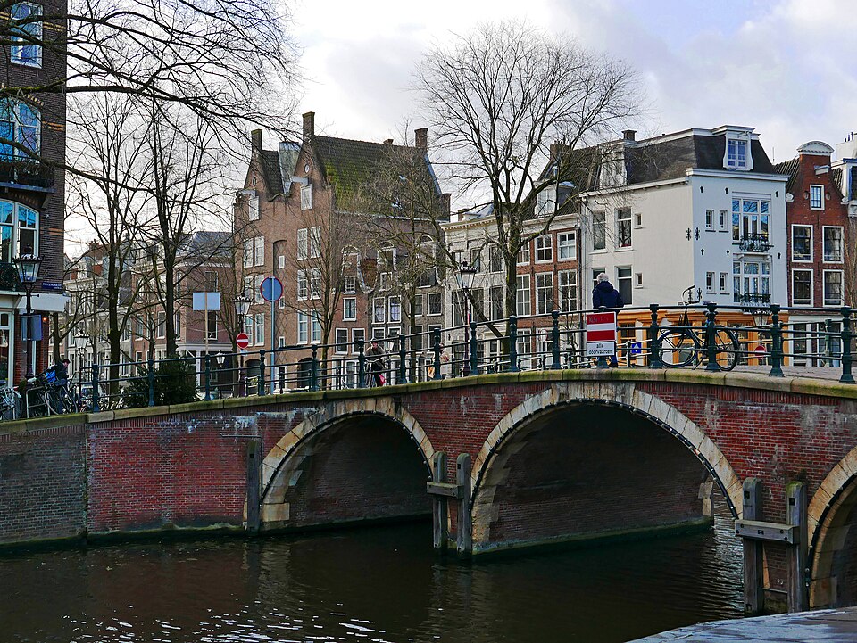 A brick arched bridge over the canal, gabled houses and bare trees behind