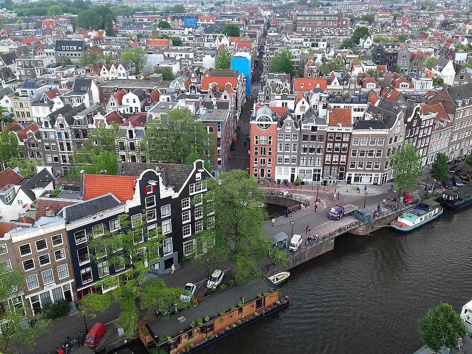 Gabled canal houses and a bridge seen from above, houseboats along the quay