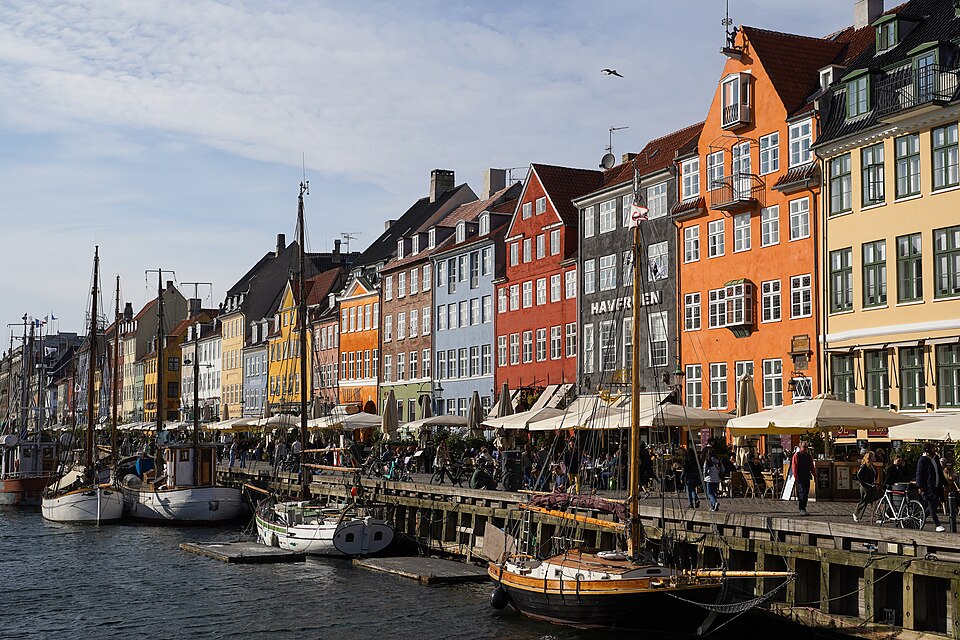 Painted gable houses and moored boats along Nyhavn, terraces below