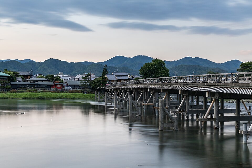 The wooden Togetsukyō bridge across the river, hills beyond at dusk