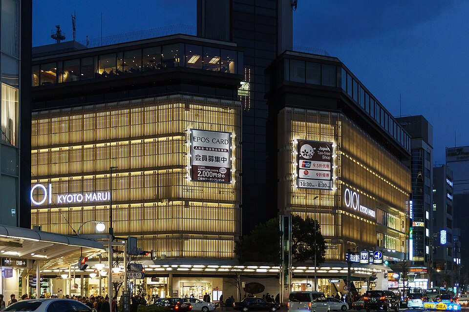 A lit department store facade on Shijō at blue hour, traffic and crowds below