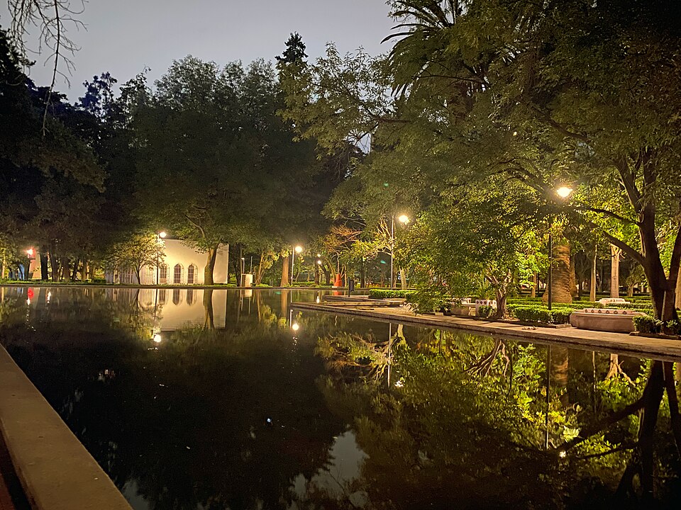 A lit reflecting pool among trees in Parque Lincoln at night