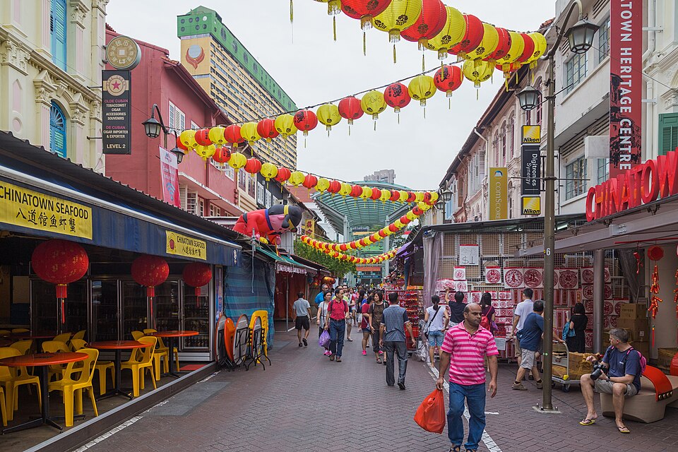 Red and yellow lanterns strung above a street of stalls and shophouses